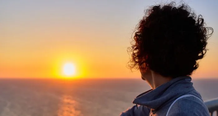 a woman with short cropped curly hair on a beach at sunset seen from behind