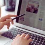 a light-skinned hand pointing at news article displayed on laptop