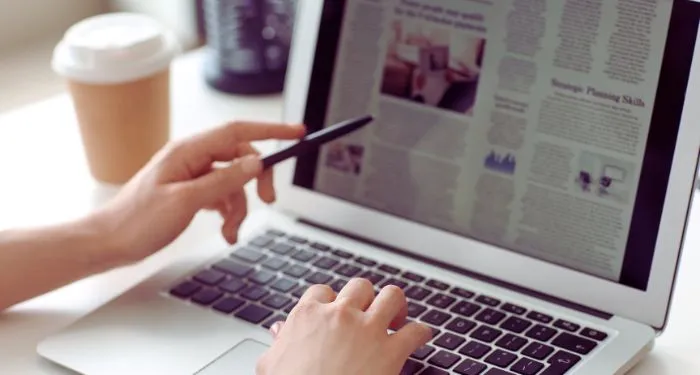 a light-skinned hand pointing at news article displayed on laptop