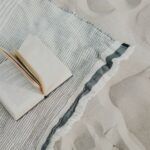 book open on a blue and white striped beach towel on sand