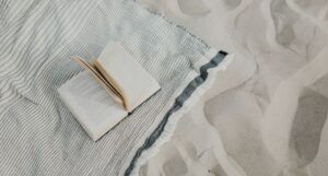 book open on a blue and white striped beach towel on sand