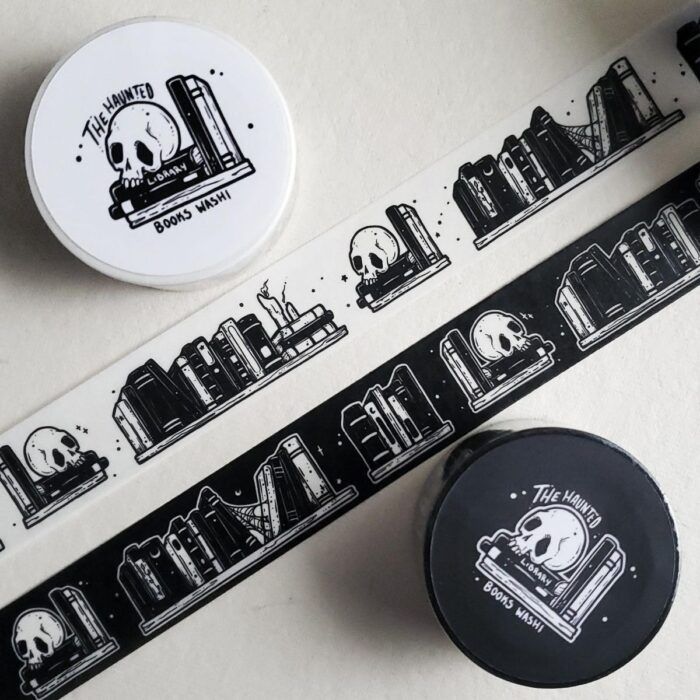 An image of two rolls of washi tape, one white, one black. The tape is unfurled down the center of the image. The tape is decorated with realistic images of skulls and books.