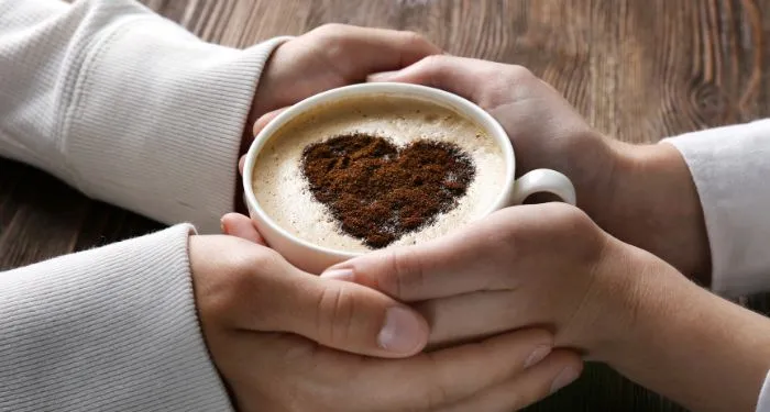 two hands holding a cup of coffee with a heart shape in the foam