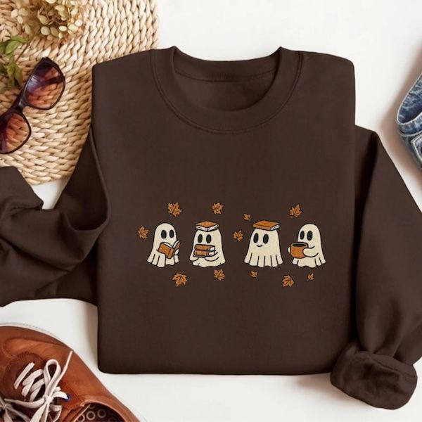 dark brown crewneck sweatshirt with an embroidered image of four ghosts on the front. Three of the ghosts are holding a book in assorted positions and one is holding a mug, with golden leaves hovering above and between all of them