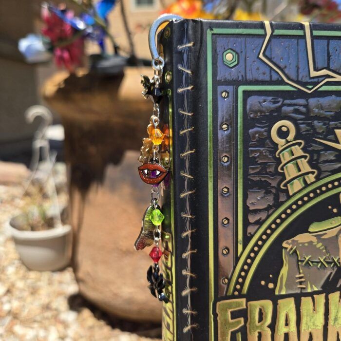 a bookmark made of a tangle of cords with beaded, Halloween-themed charms hanging out of a copy of Frankenstein 