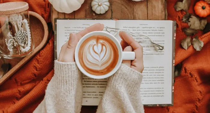 someone holding a latte with an open book and decorative pumpkins