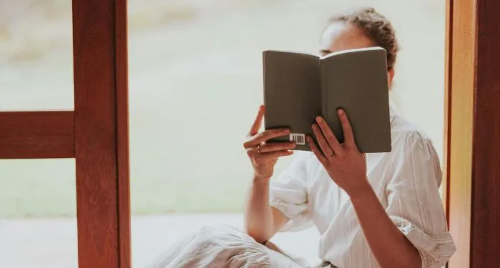a fair-skinned woman reading in a windowsill