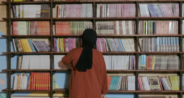 person in a head scarf looking at books on a bookshelf