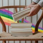 a stack of books with a rainbow watercolor ribbon in the background