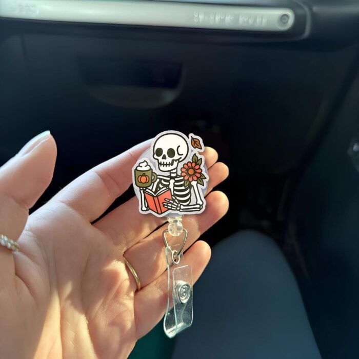 A hand holding an ID badge reel. The reel is in the shape of a skeleton holding a book.