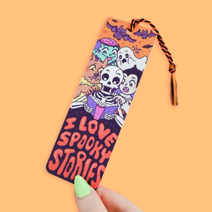 hand holding a tasselled, orange bookmark with cartoon horror figures reading and the words "I Love Spooky Stories"