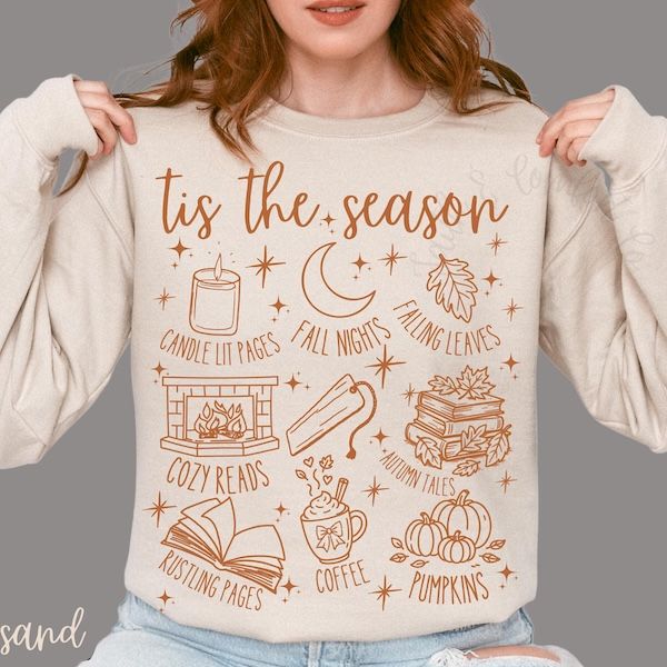 person wearing a beige sweater with fall graphics and text in orange ink. Text at the top of the design says Tis The Season and floats above nine graphics/text pairings including candle lit pages and autumn tales
