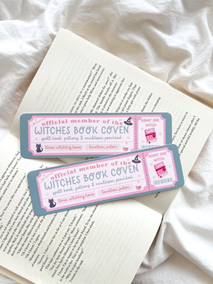 Two bookmarks laying on an open book. The bookmarks are styled like an admission ticket in pastel pinks and purples. The ticket reads "Official Member of the Witches Coven Book Club" with other details and images 