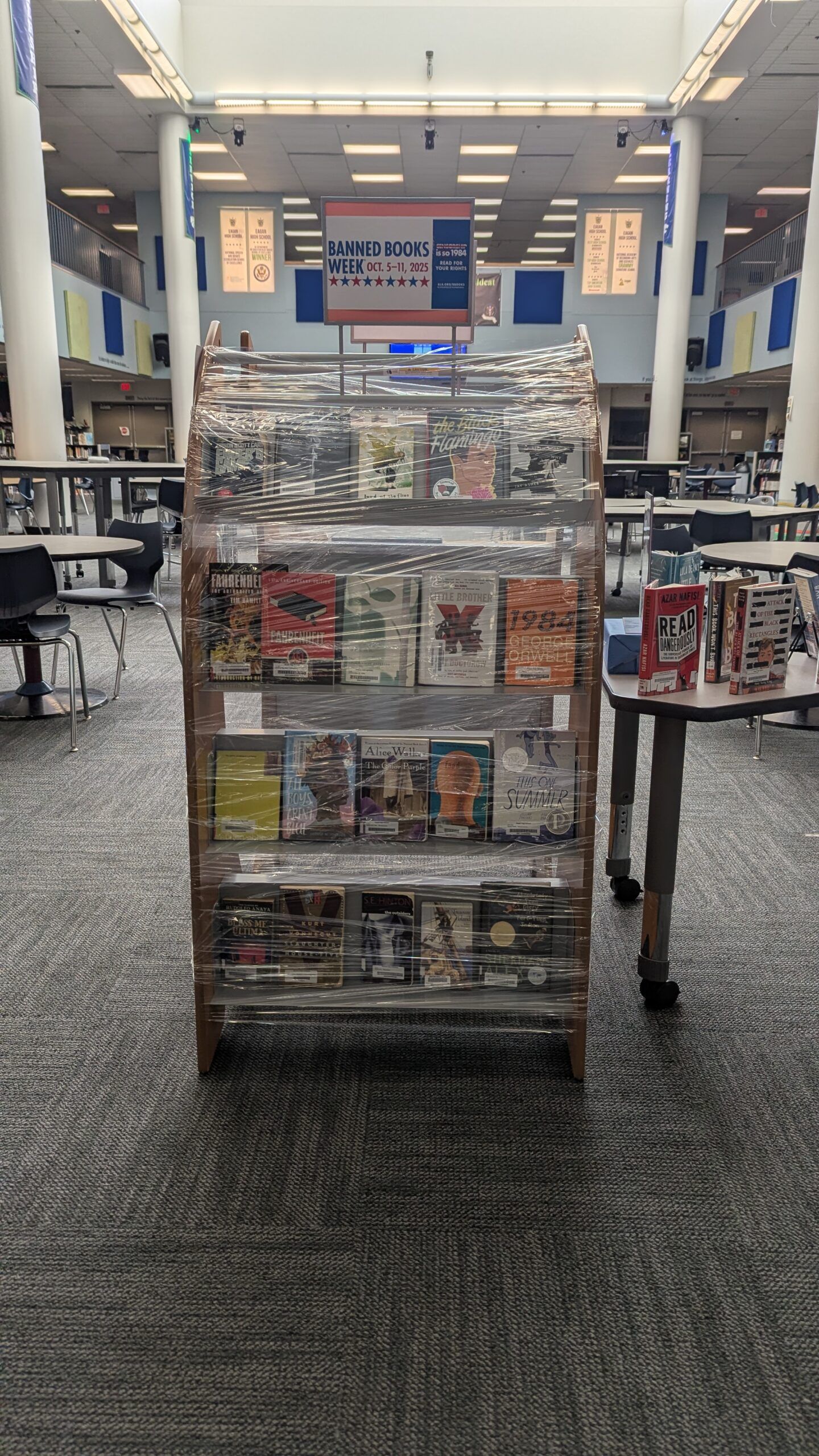 Image of a book case with banned books inside it. It is covered in saran wrap. 