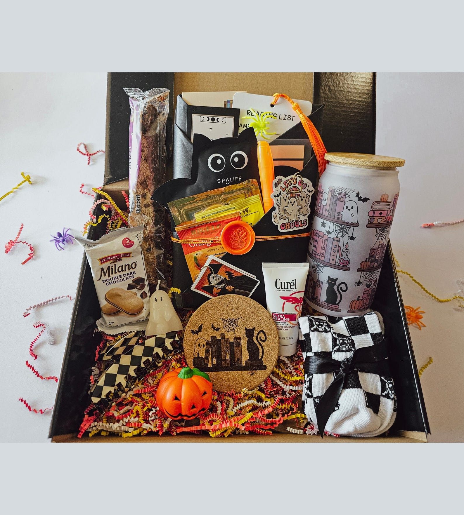 a box filled with a wrapped book and halloween-themed things like a coaster, glass, face mask, and snacks