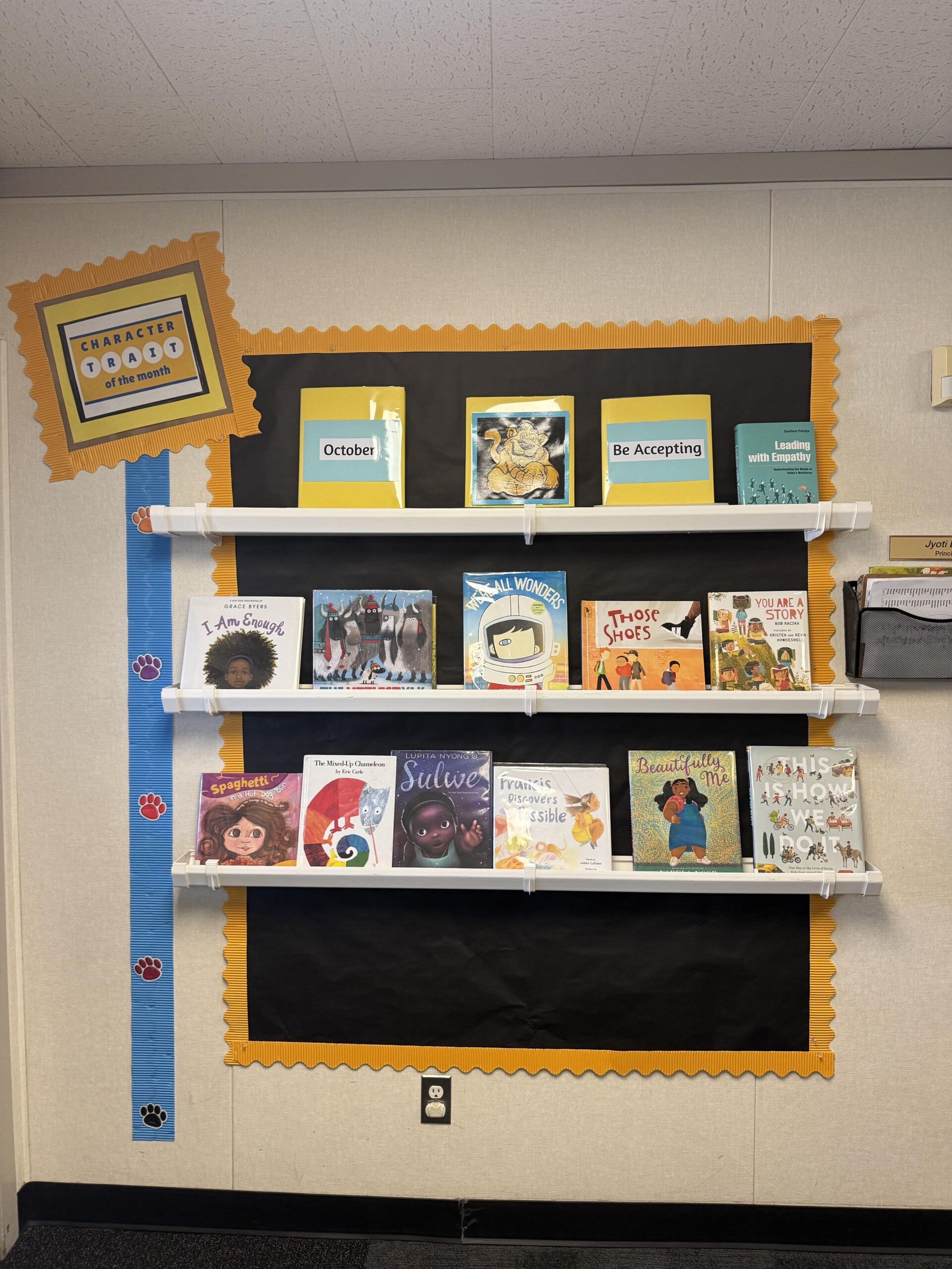 Image of a book display on a school wall. It says "Character trait of the month for October: Be accepting." There are all kinds of inclusive books on the display. 