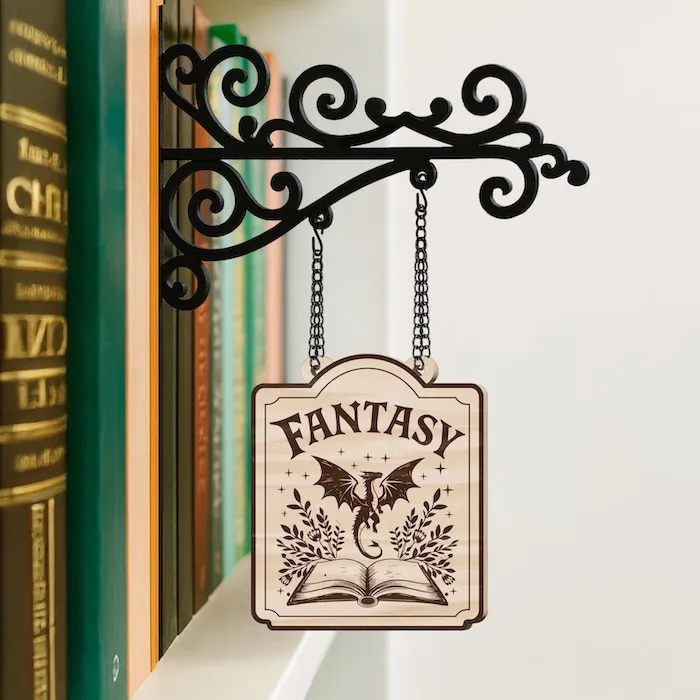 a small wooden tavern sign with the word Fantasy and a dragon hovering over a book on it. the sign is handing from an ornate metal fixture that is places between books ona shelf