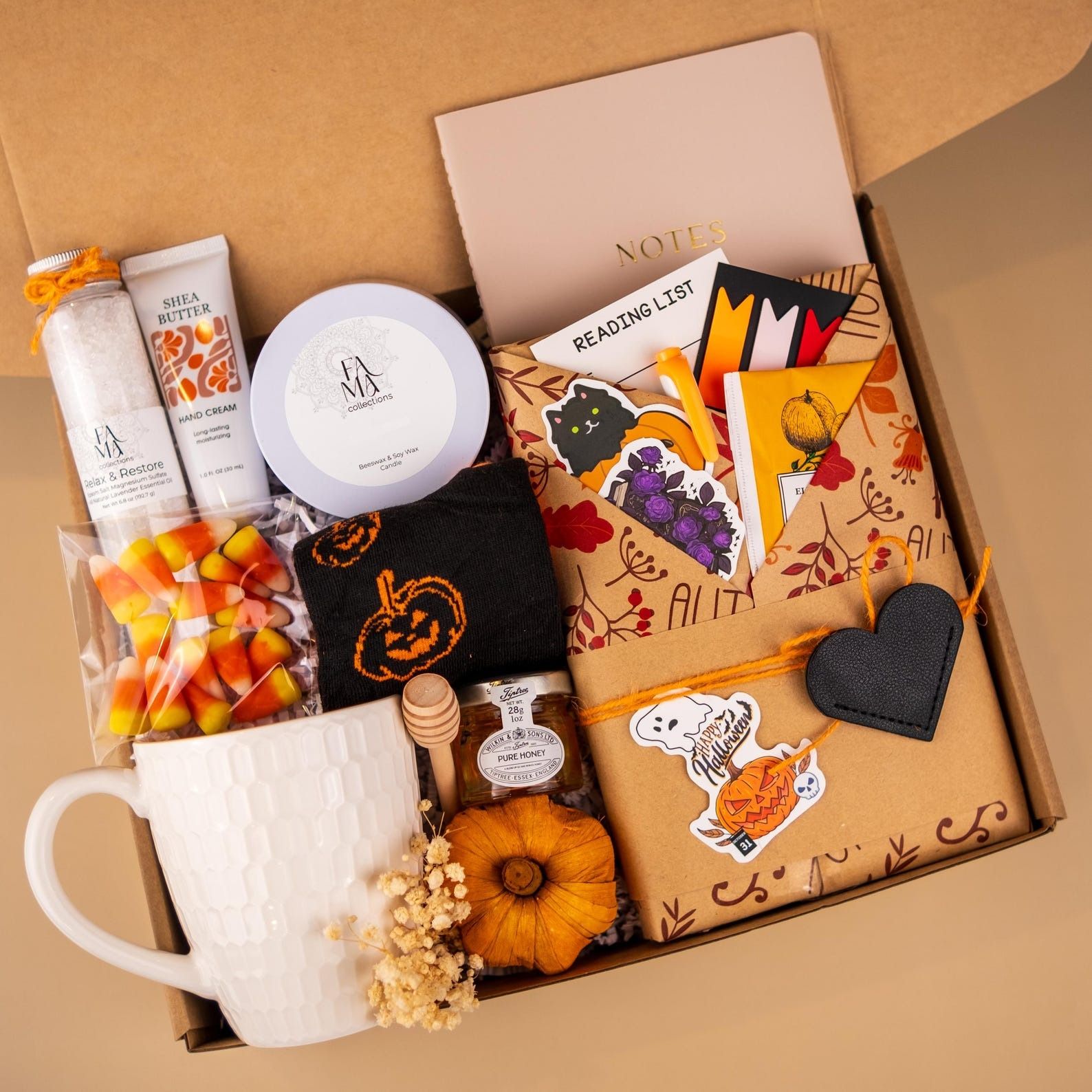 a box with a wrapped book and halloween-themed goodies, including a mug, candy corn, hand cream, socks, and honey
