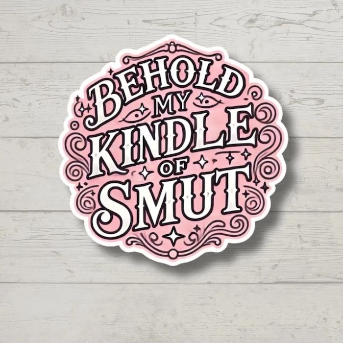a pink sticker with white text that reads Behold My Kindle of Smut