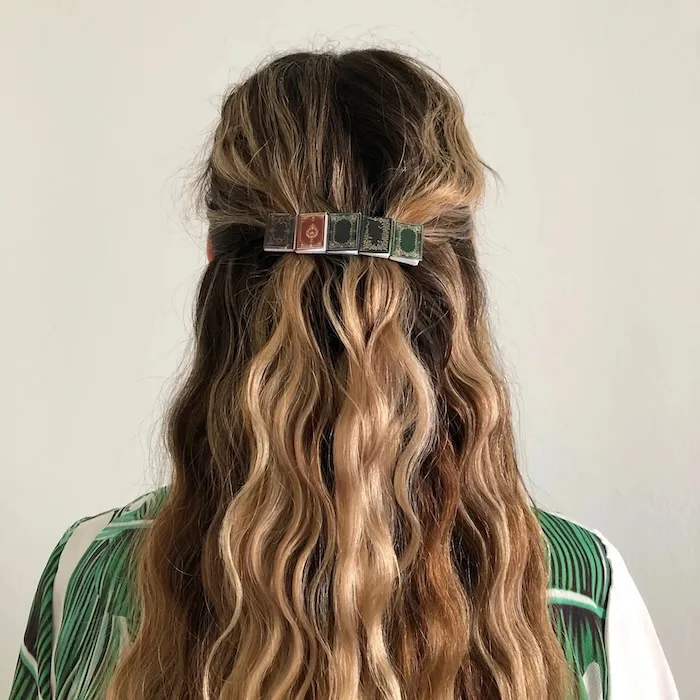 person with a half-up hairstyle with a barrette made of five small books in their hair