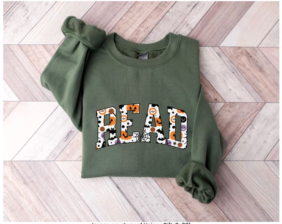 Image of an army green sweatshirt with the word "read" in white. Inside the letters is Halloween iconography. 