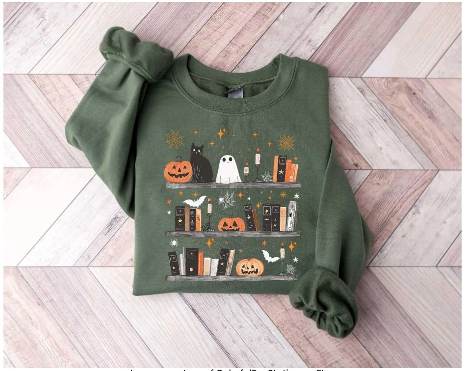Image of a green sweatshirt. It has several bookshelves on it that have cats, ghosts, books, bats, and pumpkins. 