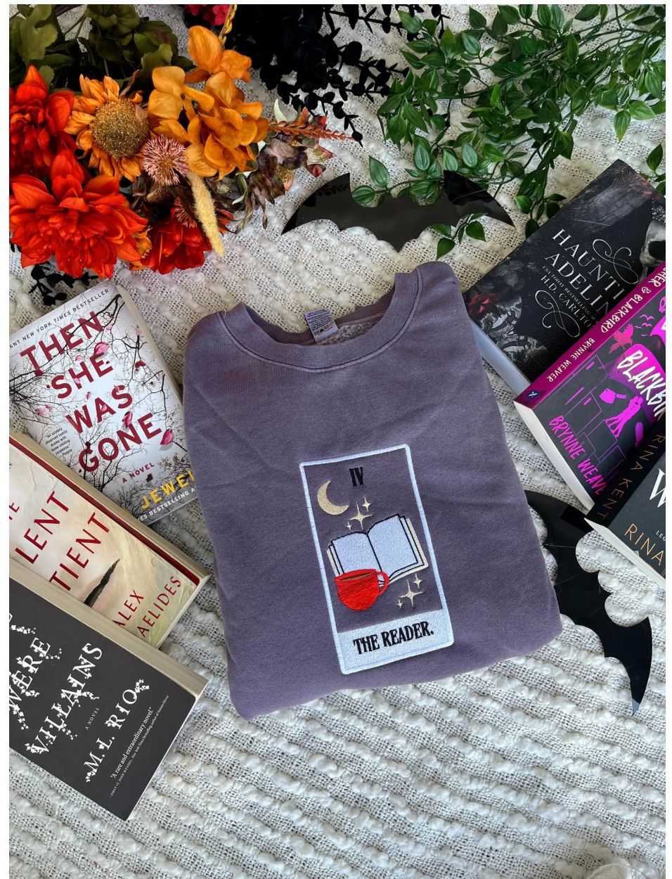 Image of a gray sweatshirt with an embroidered tarot card in the center. It is a tarot card representing "the reader," with a coffee mug, book, and half moon. 