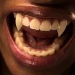 open mouth of a brow-skinned person with red lips and vampire fangs