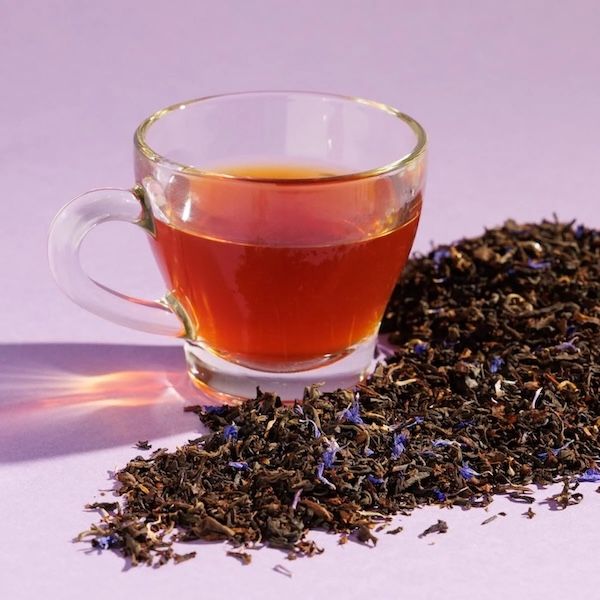 clear glass mug filled with amber-colored tea places next to a pile of loose leaf black tea 