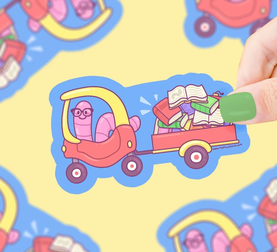 Image of a sticker. It features a worm in what looks like a kid's toy car. The car is towing a wagon full of books.