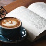 an open book with a latte and glasses beside it