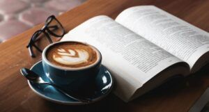 an open book with a latte and glasses beside it