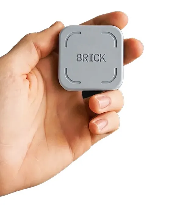 hand holding a grey plastic square with the word "brick" on it