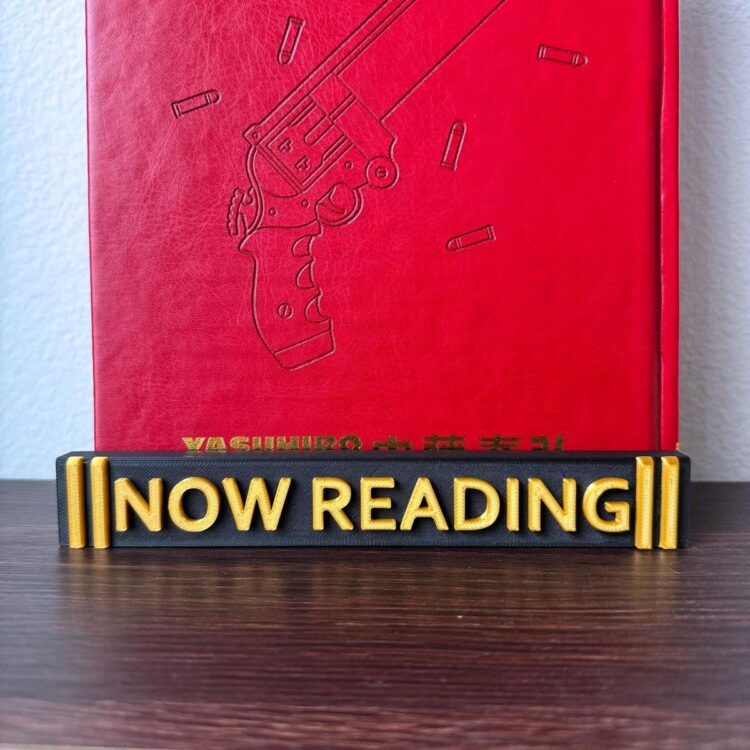 image of a red book standing in a black stand with gold details and gold words that say NOW READING