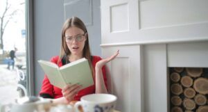 fair-skinned white woman reading a book with a surprised expression