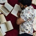 tan-skinned ban lying on a bed covered in openbooks