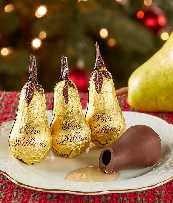 a white plate with four chocolate pears. three of them are wrapped in gold foil, one if unwrapped and open to reveal a liquer filling
