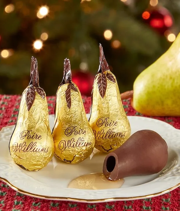 a white plate with four chocolate pears. three of them are wrapped in gold foil, one if unwrapped and open to reveal a liquer filling