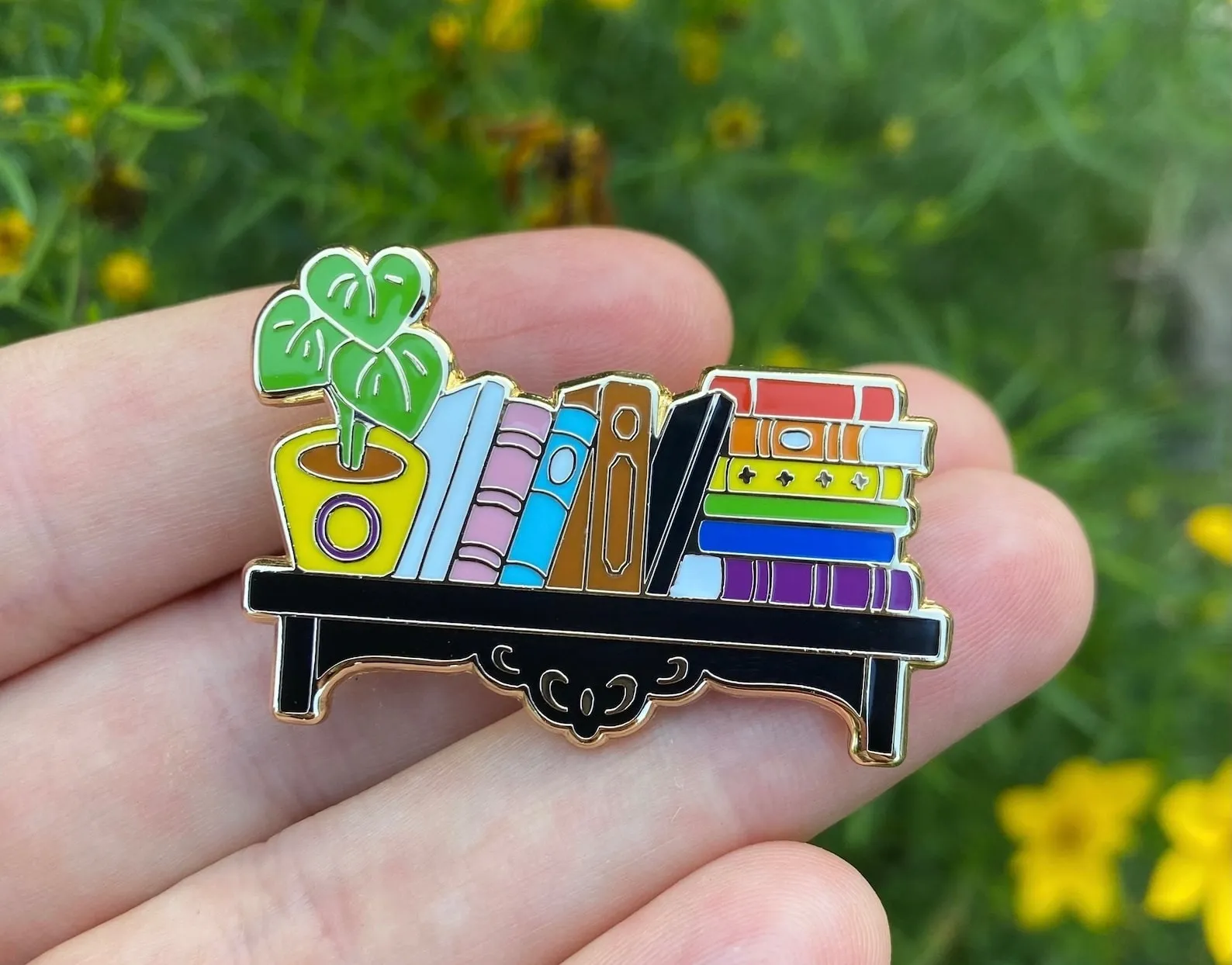 A bookshelf enamel pin in the colors of the progress pride flag