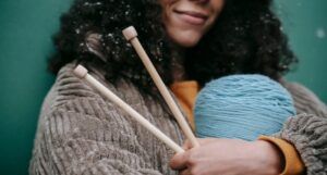 Image of a person with Brown skin hugging knitting needles and yarn