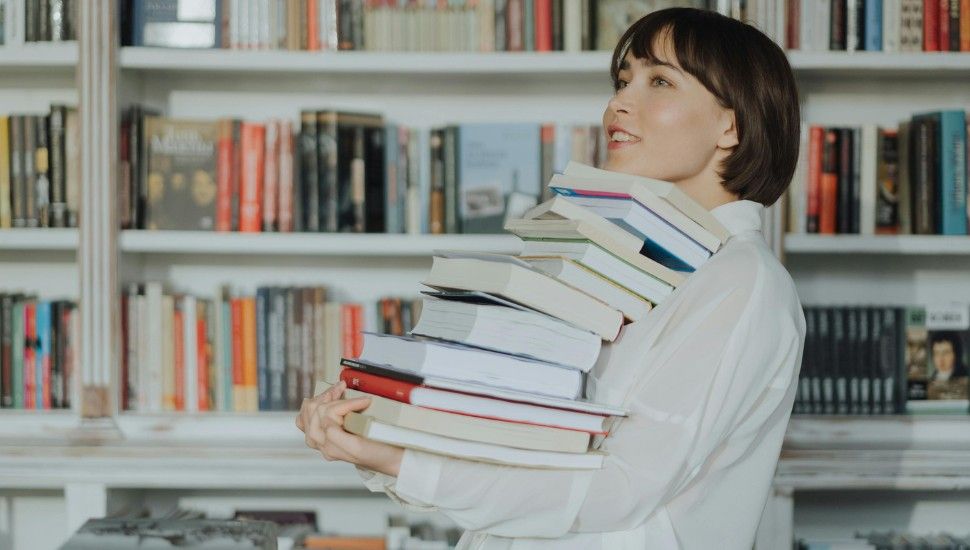 an Asian woman with light skin smiling and holding a big stack of books